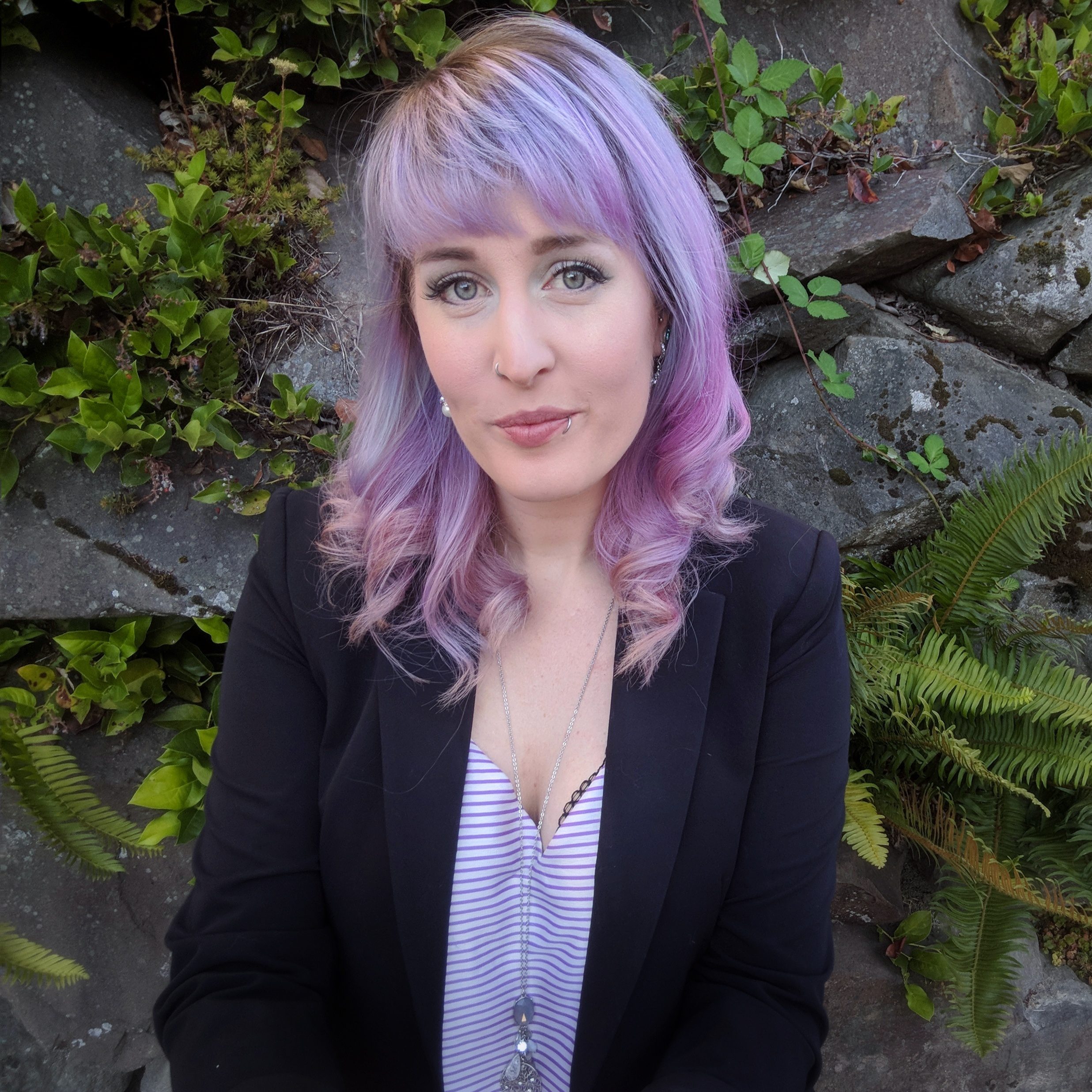 Woman with blue and purple hair earing a dark jacket and a purple and white striped shirt