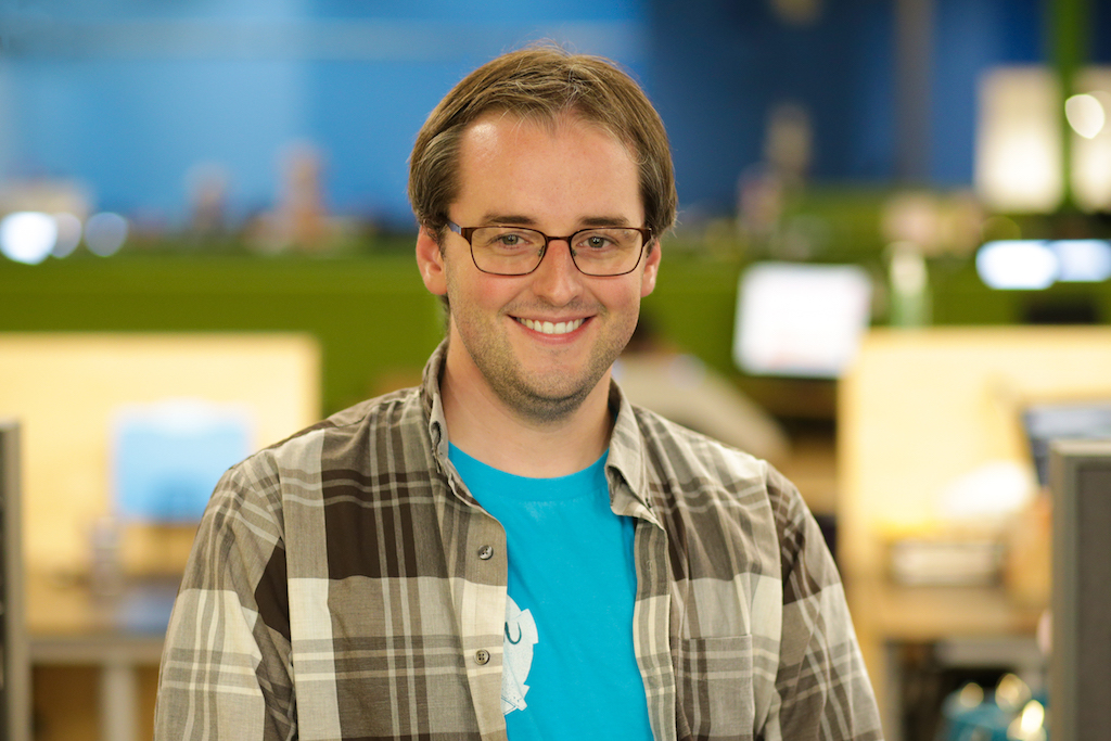 man with brown hair and glasses wearing blue shirt with flannel shirt over it
