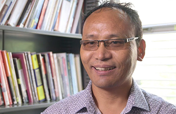 man, smiling, in front of bookshelves