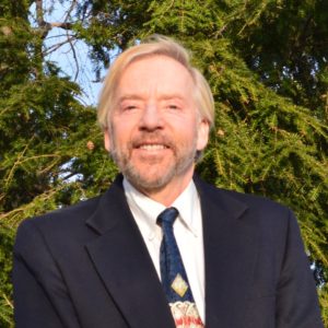 Man with short hair and beard, wearing a black suit, smiling at the camera
