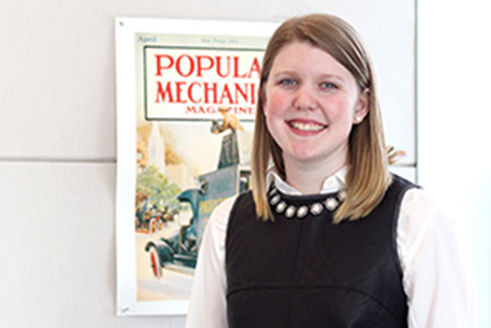 Woman with blonde/brown hair standing in front of a poster