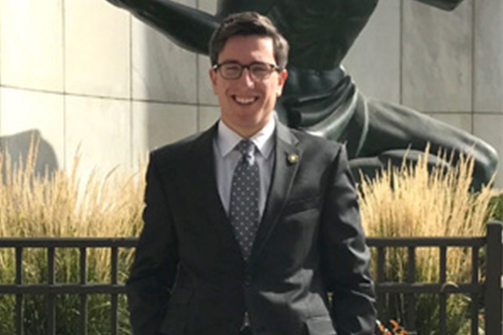Man with dark hair standing in front of a statue