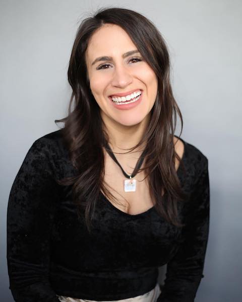 photo of a smiling woman with long, dark brown hair. she is wearing a ribbon necklace and black top