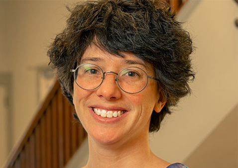 a woman smiling with dark hair, glasses, and a purple shirt