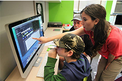 woman with dark hair teaching with two people at a computer