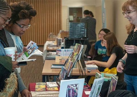 Three people standing over an organized table of comics