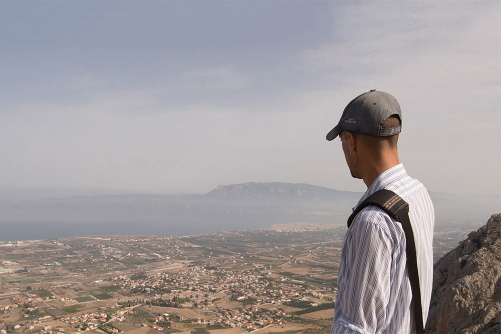 a man in a baseball cap looking out on a city from a mountain