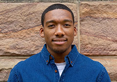 Man with blue shirt in front of brick wall