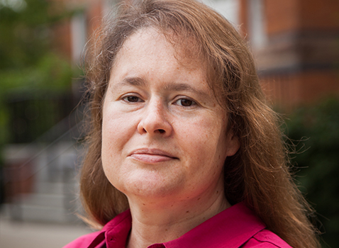 woman with long brown hair wearing a pink shirt and looking at the camera