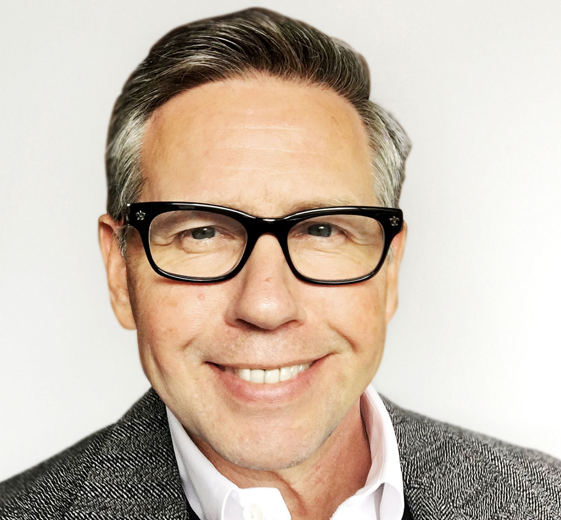 Man with brown and gray hair is wearing black rimmed glasses and a gray blazer