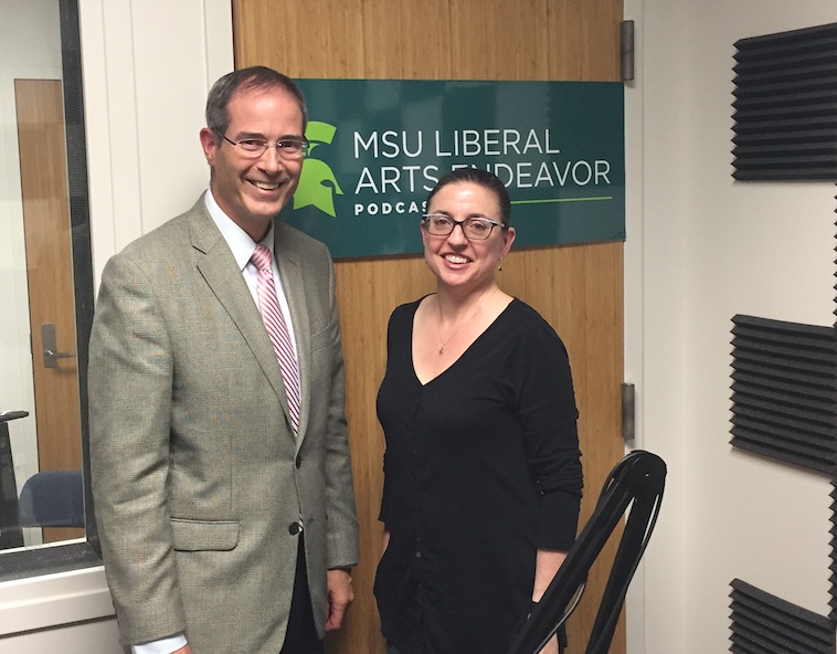 man and woman standing next to one another and smiling in front of a sign