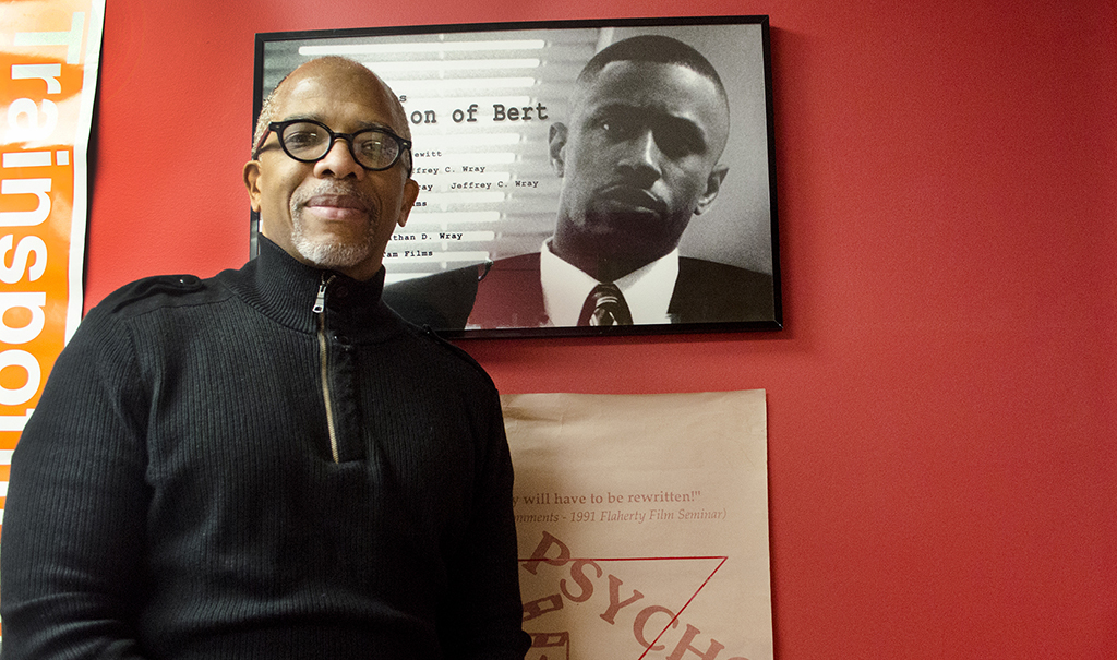 a man wearing glasses standing next to a photo of another man
