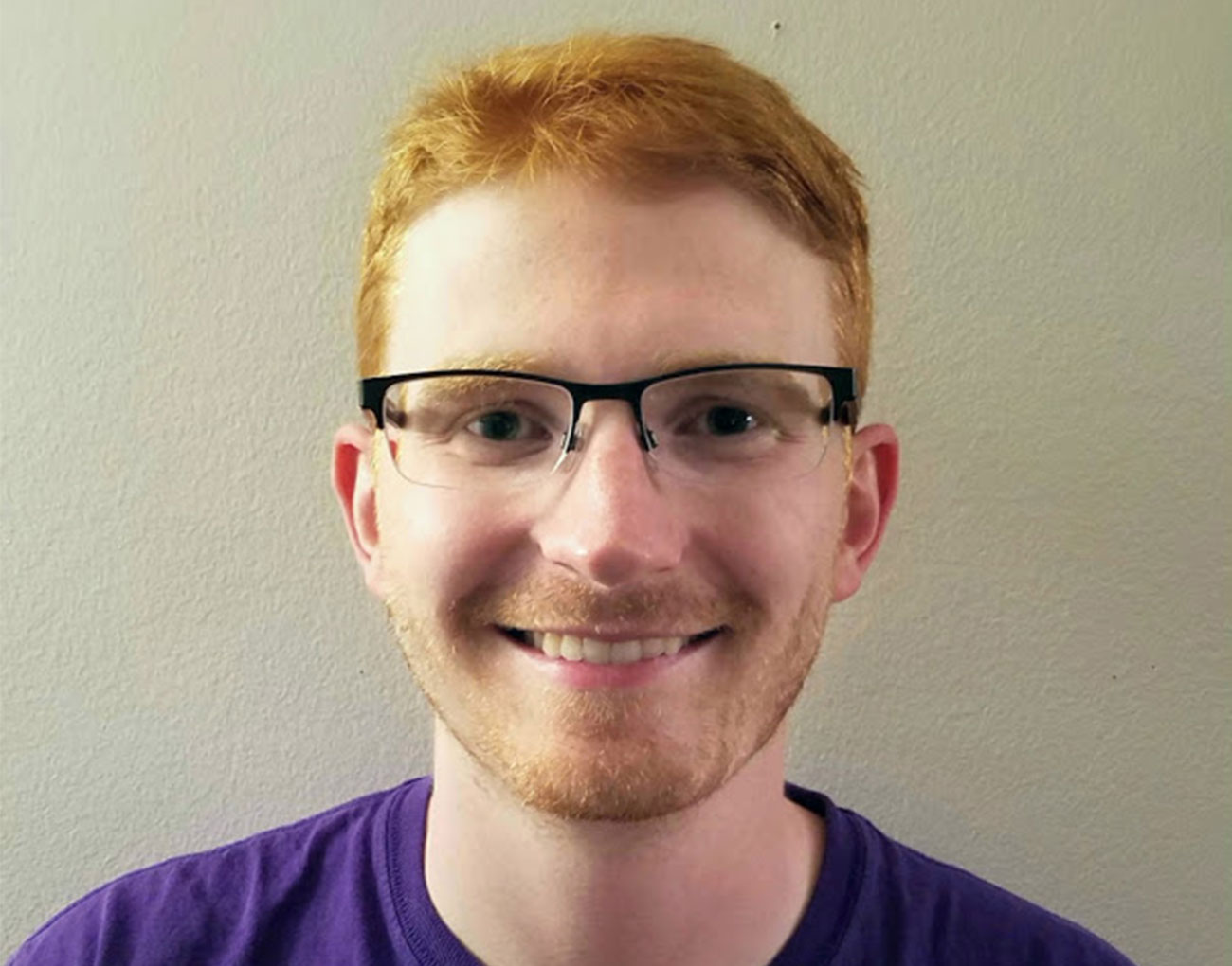 Man with red hair wearing black rimmed glasses and a purple shirt