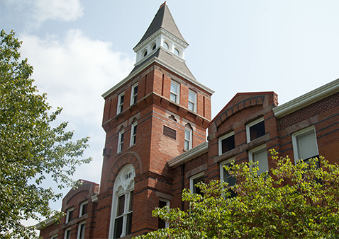 photo of an orange brick building with a clock tower in front of a cloudy sky and green trees