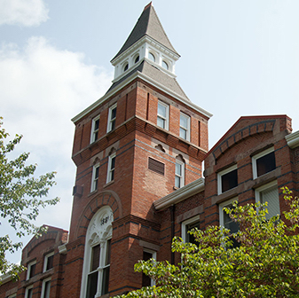 Brown brick building surrounded by green and red trees in front of blue sky