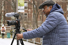 man standing with camera tripod on bridge on msu campus
