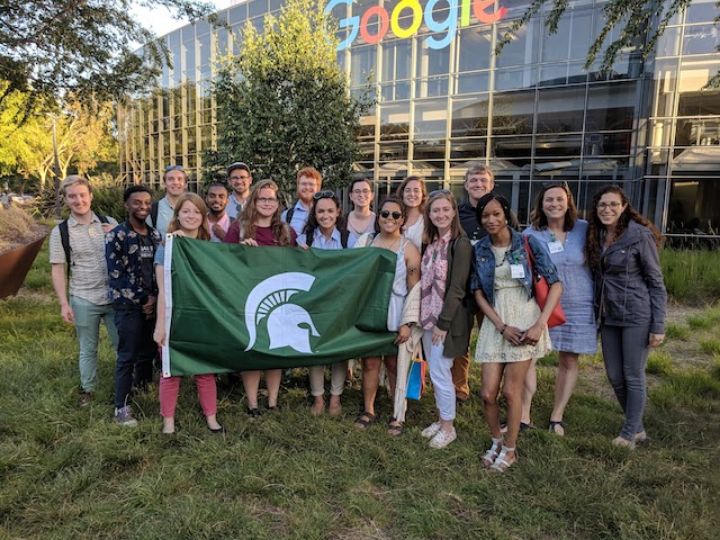 large group in front of google building holding a MSU flag