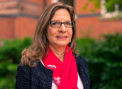 woman with brown hair wearing glasses a bright pink scarf and navy blue jacket