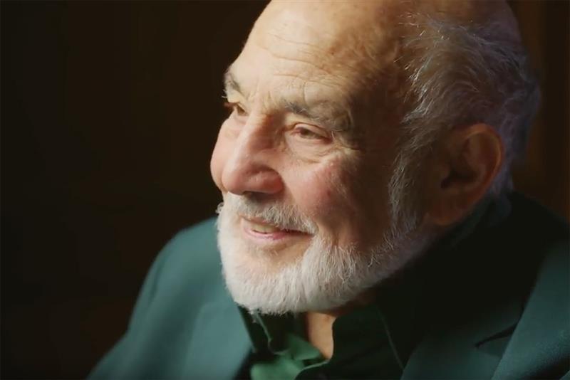 a man with a white beard wearing a green shirt smiling
