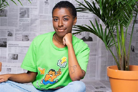 a person with short hair, sitting down wearing a green shirt and blue jeans