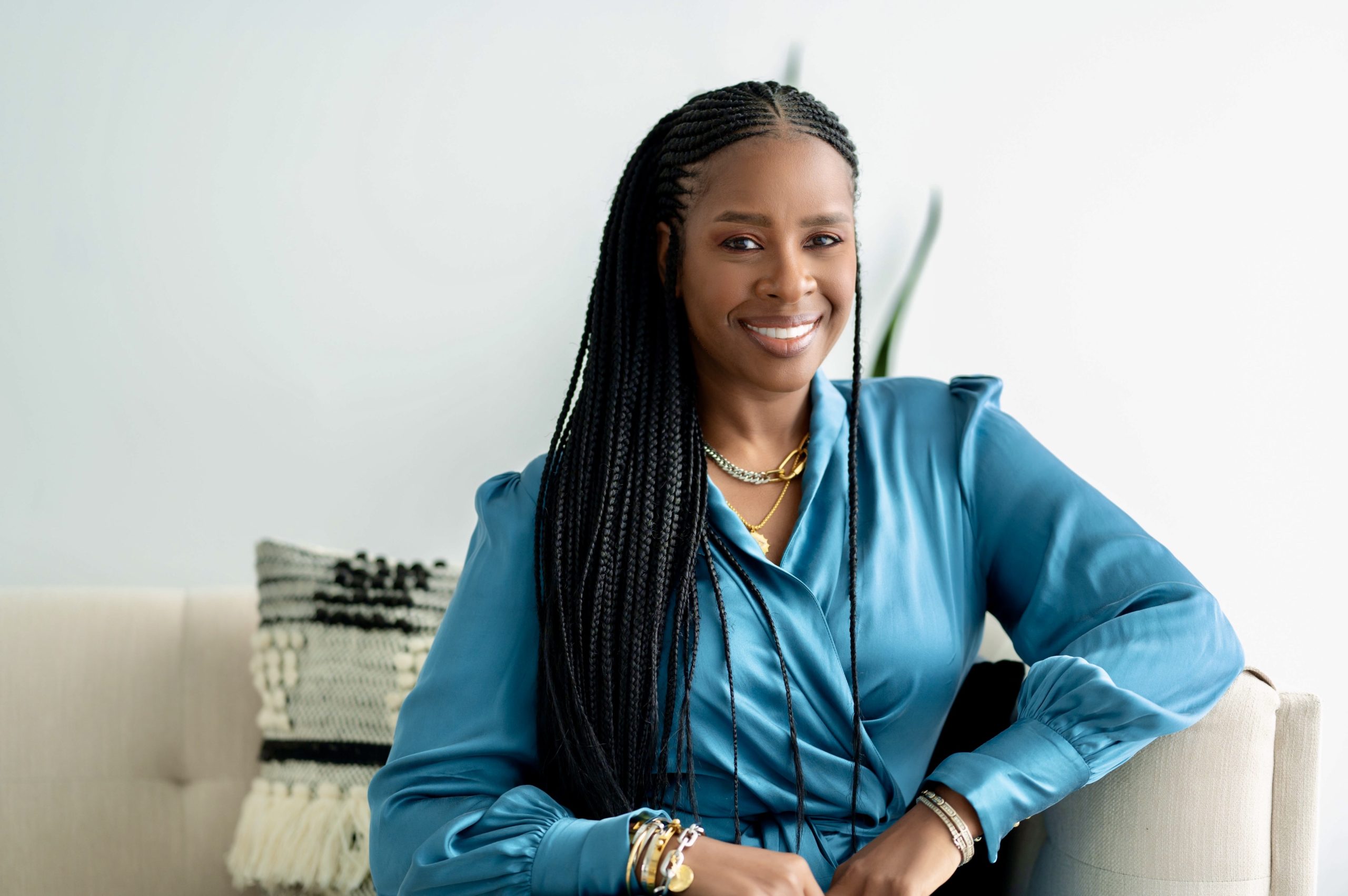 Headshot of Tamura Lomax wearing a blue shirt and sitting on a white couch..