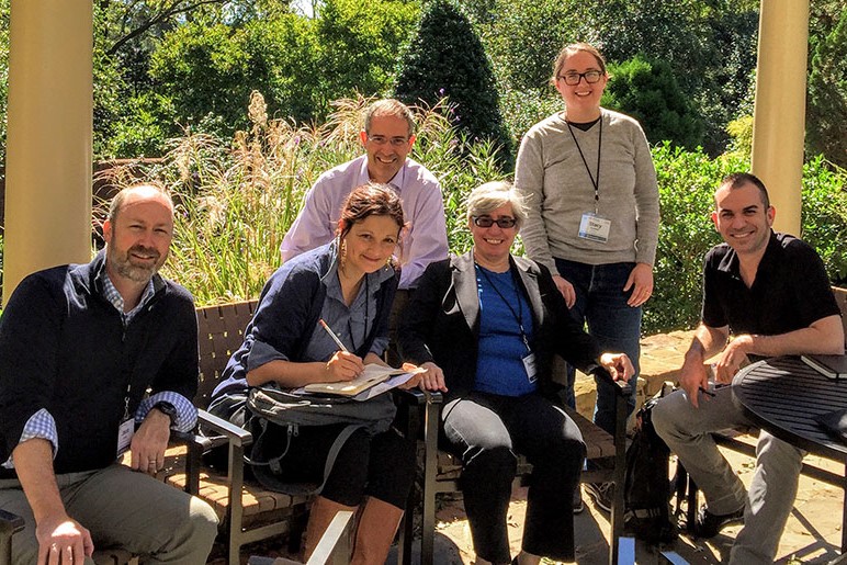 Original HuMetrics Team sitting outside on a patio at the Rizzo Center in Chapel Hill, NC. From left to right is Jason Rhody, Nicky Agate, Chris Long (sitting in the back), Rebecca Kennison, Stacy Konkiel (standing in the back), and Simo Sacchi.