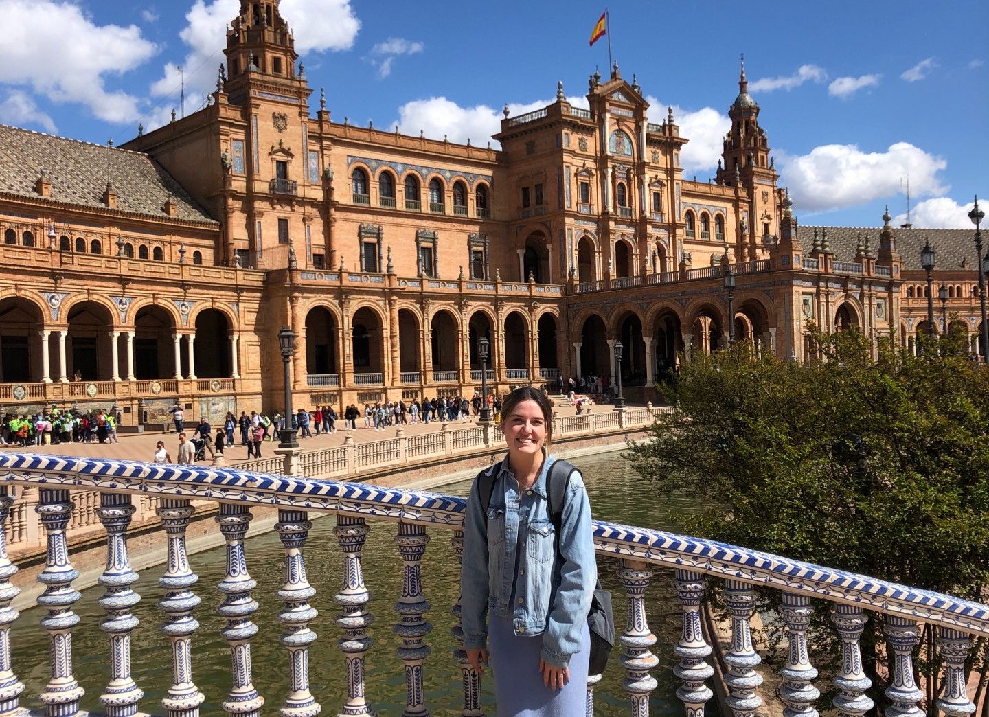 Person smiling outside with a large castle-like building behind them with old architecture.