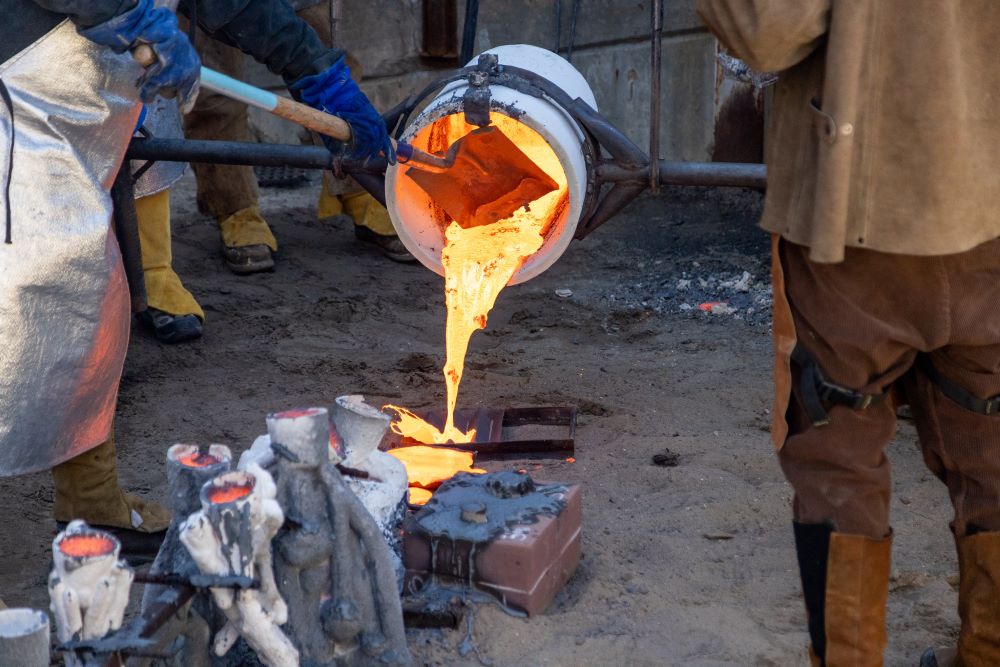 Molten metal pours out of a crucible into molds in an outdoor setting.