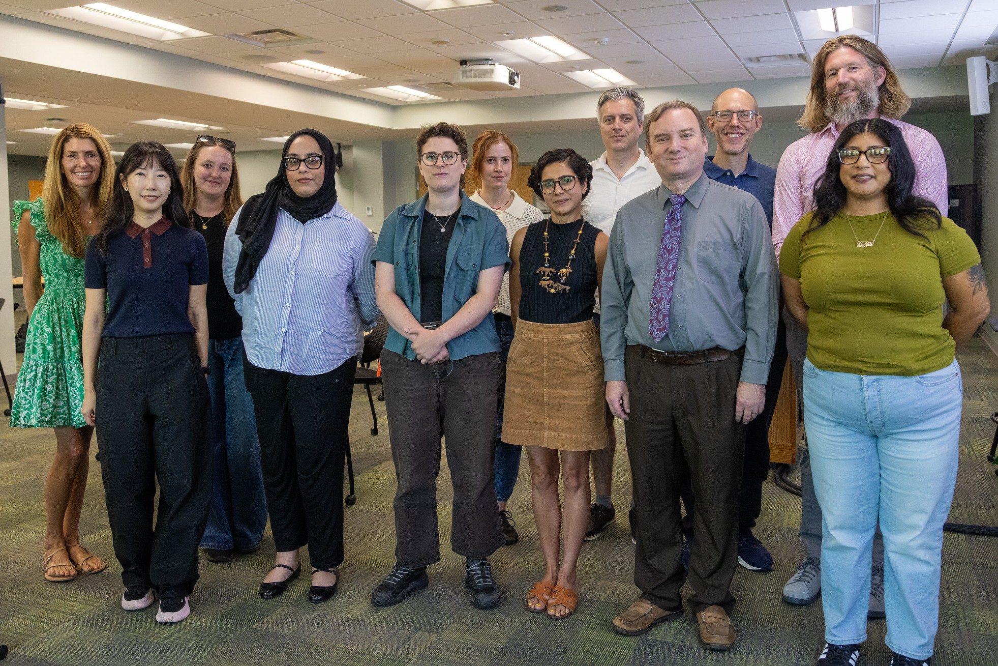 A group of 12 new faculty and staff members pose together for a photo in a meeting room at Michigan State University.
