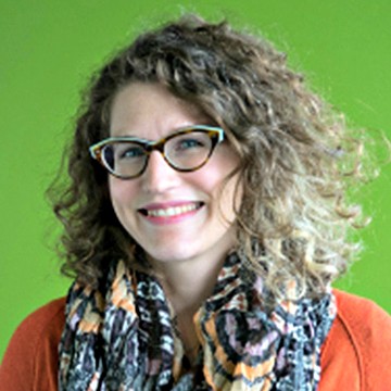 Headshot of a smiling woman with curly hair and cat-eye glasses, wearing an orange top and a patterned scarf against a bright green background.