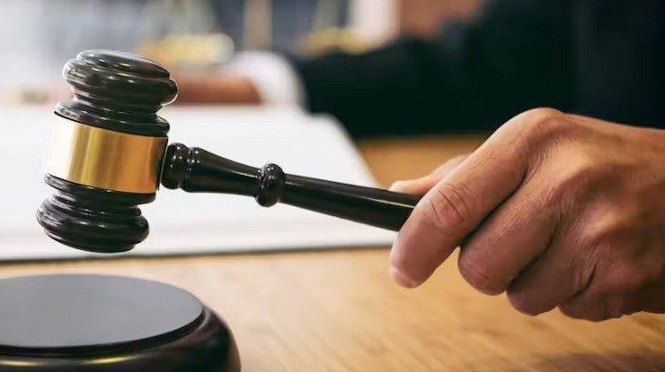 A hand holding a wooden judge’s gavel above a sound block on a desk.