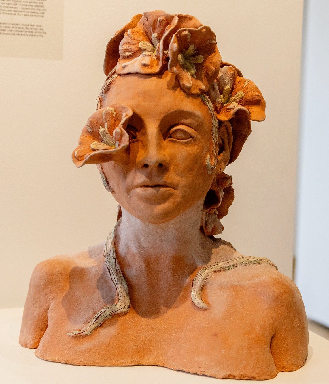 Terracotta bust of a woman with sculpted flowers surrounding her head and face.