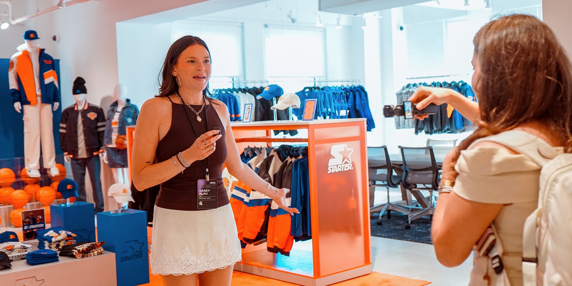 MSU student Casey Klau speaks during a visit to the Starter showroom in New York City as another participant takes her photo. Sports apparel and merchandise are displayed throughout the showroom.