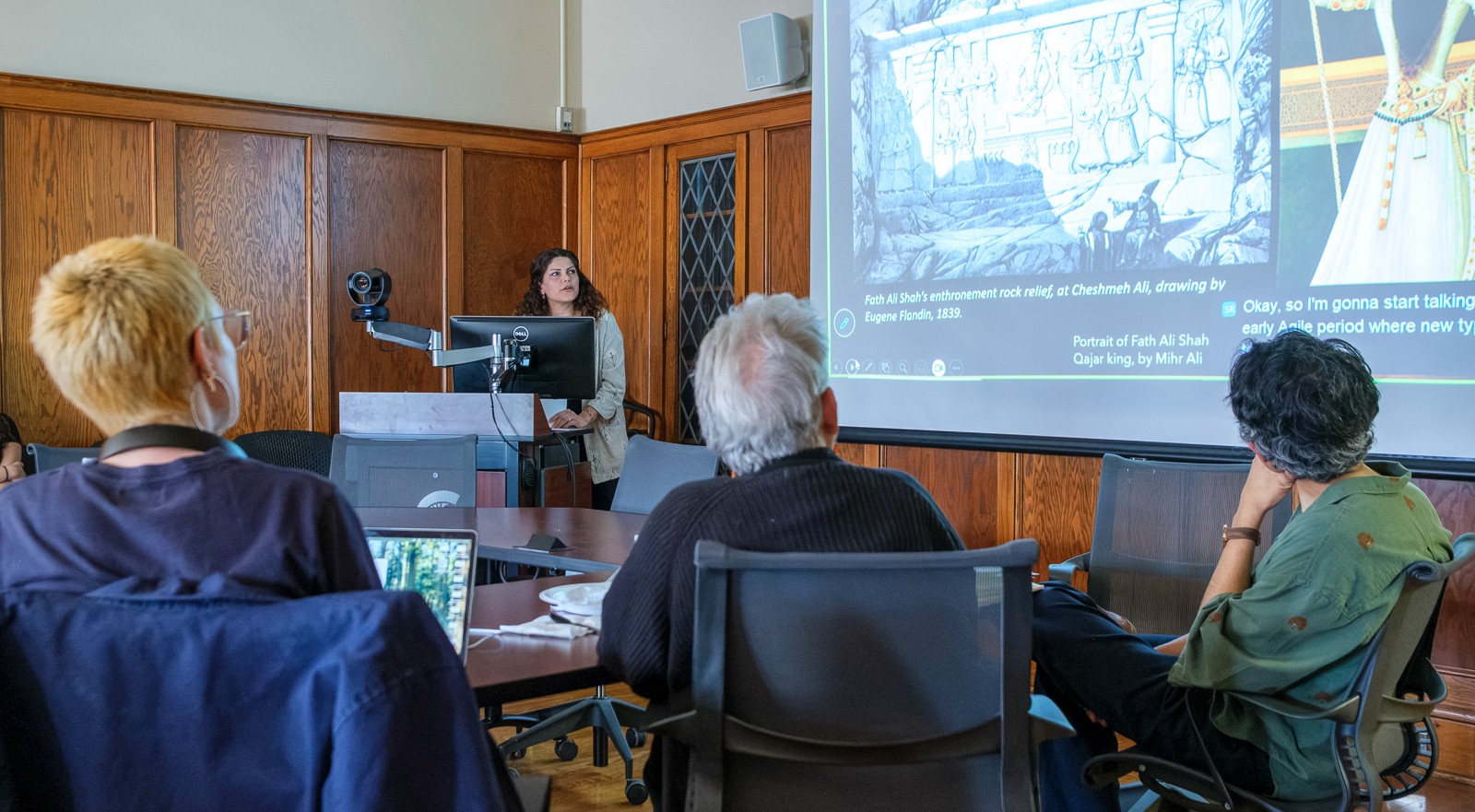 Samira Fathi delivers a presentation on early modern Persian art and architecture to an audience in a wood-paneled conference room, with historical images projected on a screen.