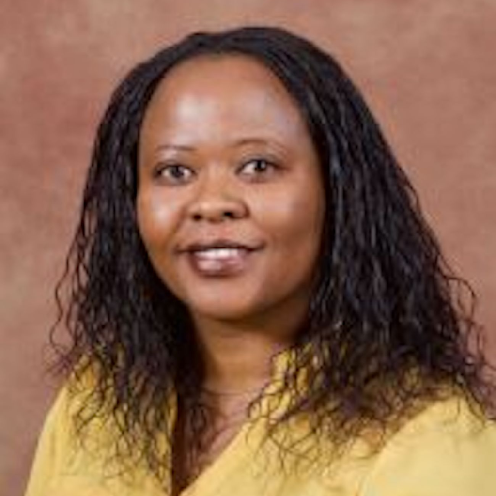 Dr. Esther Milu wearing a yellow blouse against a brown background.