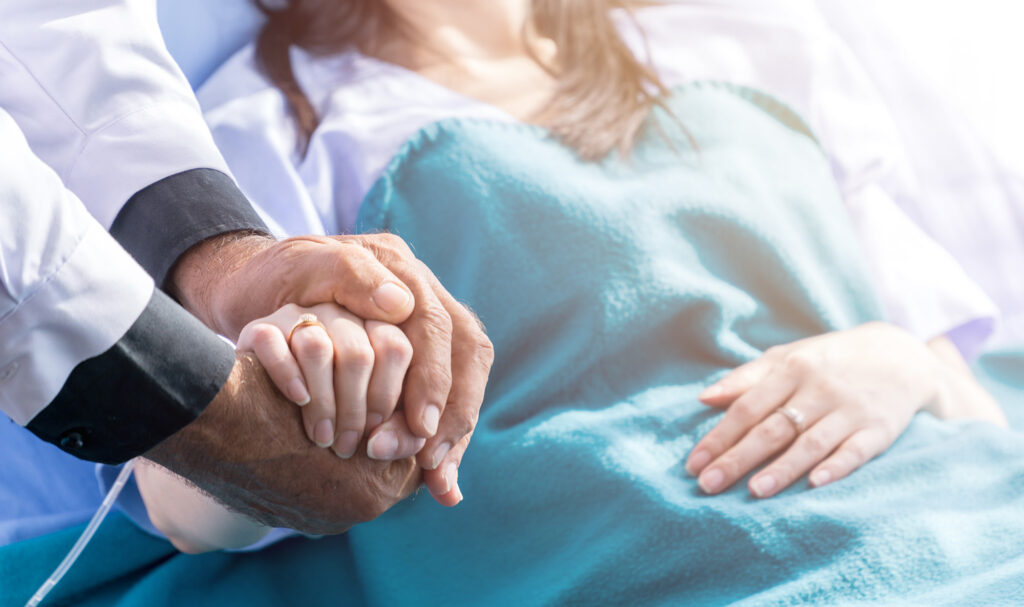 Close up image of healthcare provider holding a patient’s hand in a hospital bed.